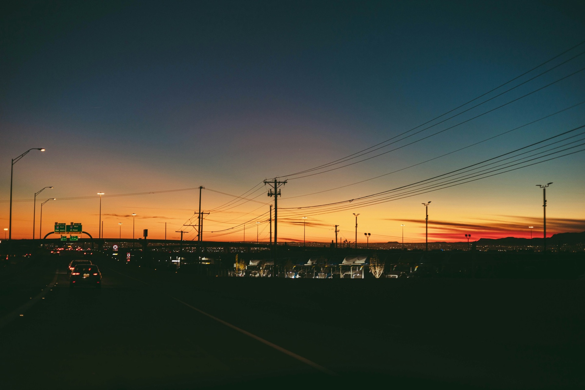 Sun setting behind a Texas city skyline framed by high-voltage power lines, representing the shifting commercial electricity market discussed at EMC25 Houston.